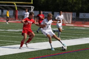 Soccer players in action on the field, one in red and one in white, competing for the ball near the goal.