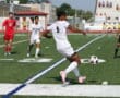 Soccer player in white jersey controlling ball on field during match, with referee and opponents in background.