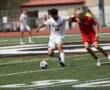 Two soccer players compete for the ball on a sunny day on a high school field.
