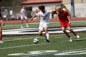 Two soccer players compete for the ball on a sunny day on a high school field.