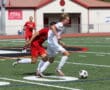 Soccer players in action on the field during a competitive game, wearing red and white uniforms.