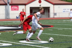 Soccer players in action on the field during a competitive game, wearing red and white uniforms.