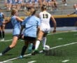 Girls' soccer match action with players competing for the ball on a sunny day.
