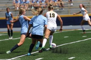 Girls' soccer match action with players competing for the ball on a sunny day.