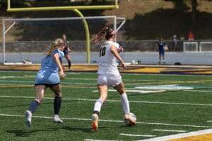 Two female soccer players compete for the ball on a sunny field, focusing on control and agility.