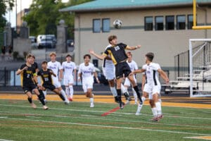Soccer players in action on the field, mid-air jump for the ball during a high school match.