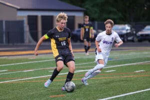 Two soccer players from opposing high school teams compete for control of the ball on the field.