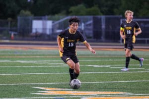 Soccer player in black and yellow uniform dribbling ball on green field during a match.