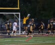 Soccer goalie catches a ball during a match, with players surrounding the goal post in a night game setting.