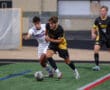 Two soccer players competing for the ball during a high school match on a green field.