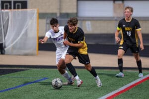 Two soccer players competing for the ball during a high school match on a green field.