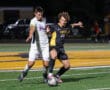 Two soccer players competing for the ball during a night match on a brightly lit field.