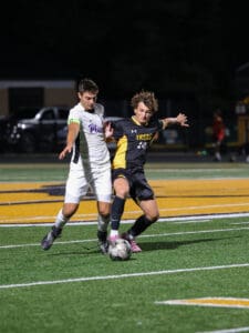 Two soccer players competing for the ball during a night match on a brightly lit field.