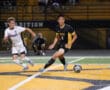 Two soccer players compete for the ball during a night match on a brightly lit field.