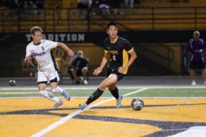 Two soccer players compete for the ball during a night match on a brightly lit field.