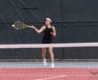 Tennis player hitting a forehand shot on a court, wearing a visor and black sportswear.