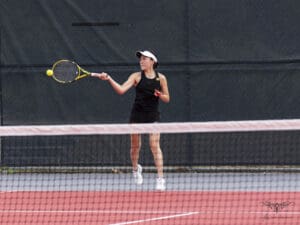 Tennis player hitting a forehand shot on a court, wearing a visor and black sportswear.