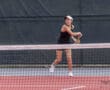 Tennis player preparing to hit a forehand shot on a red court with a net in the foreground.