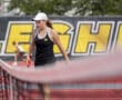 Tennis player in action at a match, holding a racket with determination, logo in the background.