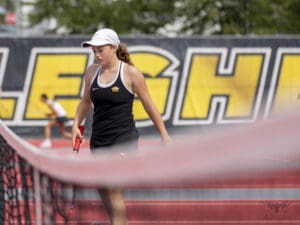 Tennis player in action at a match, holding a racket with determination, logo in the background.
