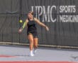 Tennis player hitting a forehand shot on a court with a sports medicine banner in the background.