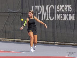 Tennis player hitting a forehand shot on a court with a sports medicine banner in the background.