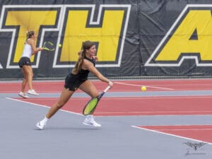 Two female tennis players in action on a bright red court, focusing on returning a tennis ball.