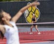 Tennis player prepares to return serve during a match on a bright red court, with a logo in the background.