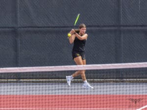 Tennis player in mid-swing during a match on a court with a net in the foreground.