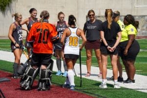 Field hockey team during a match break, players listening to coaches on a sunny day.