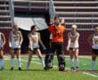 Field hockey team in white and orange uniforms, standing on the field, preparing for a game.