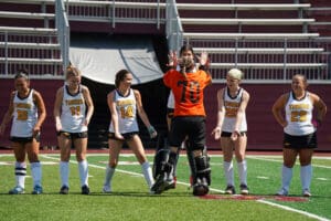 Field hockey team in white and orange uniforms, standing on the field, preparing for a game.