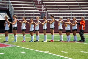 Field hockey team standing in line on a field, wearing uniforms and preparing for the game.