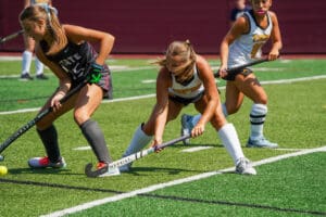 Field hockey players in action on a sunny day, competing intensely on the grass field.