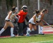 Field hockey players defend the goal during a match, wearing team uniforms and protective gear.