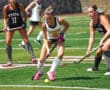 Field hockey players compete for the ball on a sunny day, displaying skills and teamwork on the green turf.