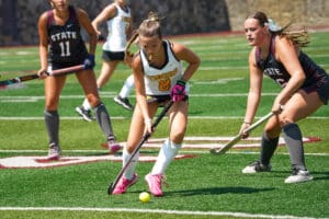 Field hockey players compete for the ball on a sunny day, displaying skills and teamwork on the green turf.