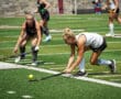 Two field hockey players in action, competing intensely on a sunny day at a green turf field.