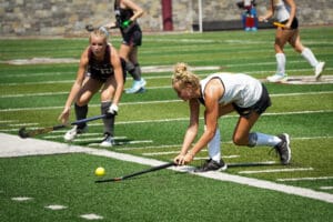Two field hockey players in action, competing intensely on a sunny day at a green turf field.