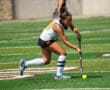 Field hockey player in action, dribbling ball on green turf during a sunny match.