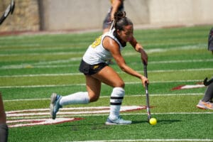 Field hockey player in action, dribbling ball on green turf during a sunny match.