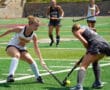 Two female field hockey players competing for the ball on a sunny day.