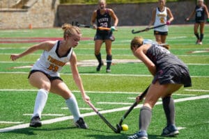 Two female field hockey players competing for the ball on a sunny day.