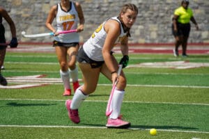 Field hockey player in action on the field, focusing on ball control while teammates follow.