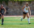 Two field hockey players competing intensely on a green field, one wearing State jersey, the other Tigers.