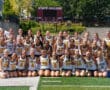 Girls' field hockey team posing on the field, wearing Tigers jerseys, in front of a scoreboard at State College.