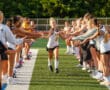 Field hockey player running through cheering teammates on a sunny day.