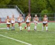 Girls' field hockey team running on a green field, wearing Tigers uniforms, showing team spirit.