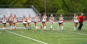 Girls' field hockey team running on a green field, wearing Tigers uniforms, showing team spirit.