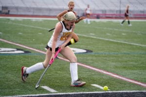 Field hockey player dribbling with a bright pink stick during a match on a green turf field.